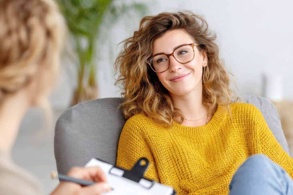 Young woman smiling during therapy session with psychologist taking notes