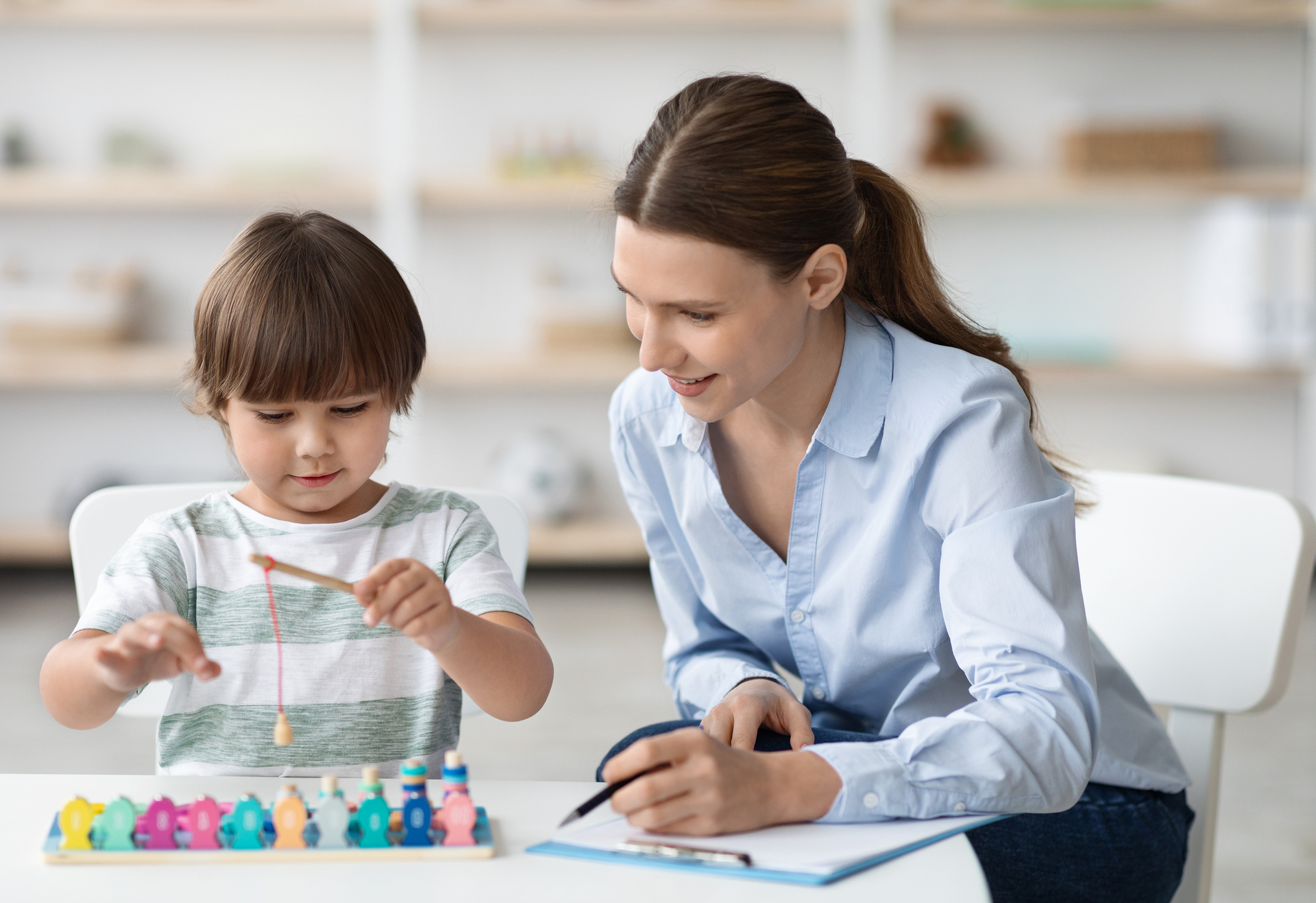 Early development concept. Happy little boy playing with wooden fishing game during psychological session